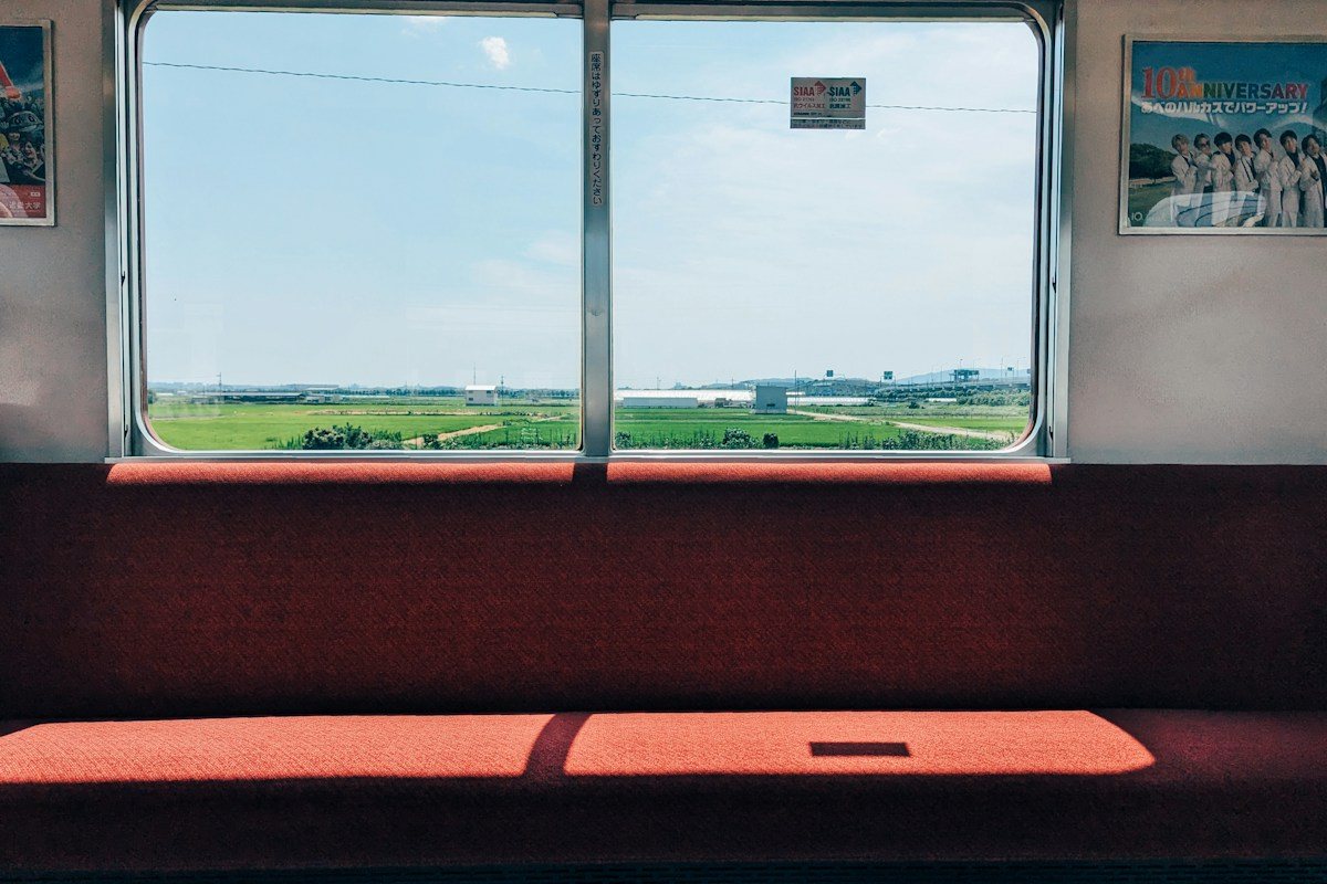 Green fields outside a train window above a red upholstered seat