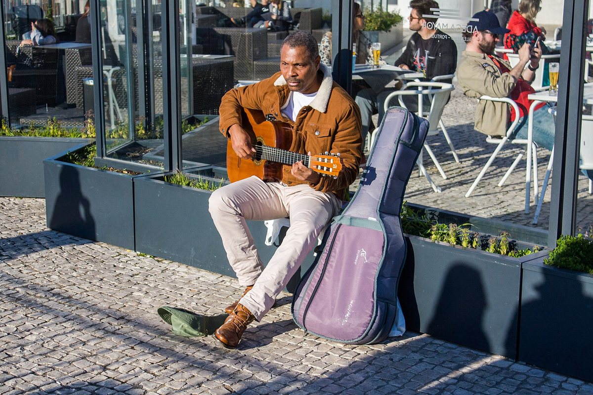 A seated guitarist plays beside his open case on a Lisbon street